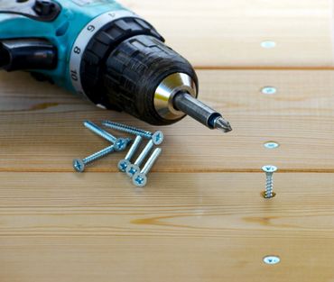 A cordless drill is placed on a wooden surface with several screws.