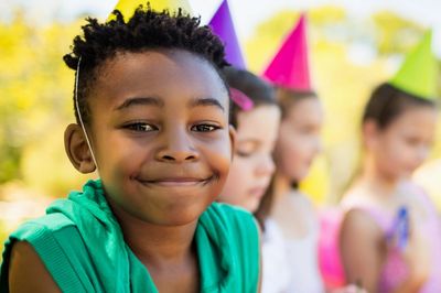 Smiling child at a colorful birthday party with friends and cupcakes.