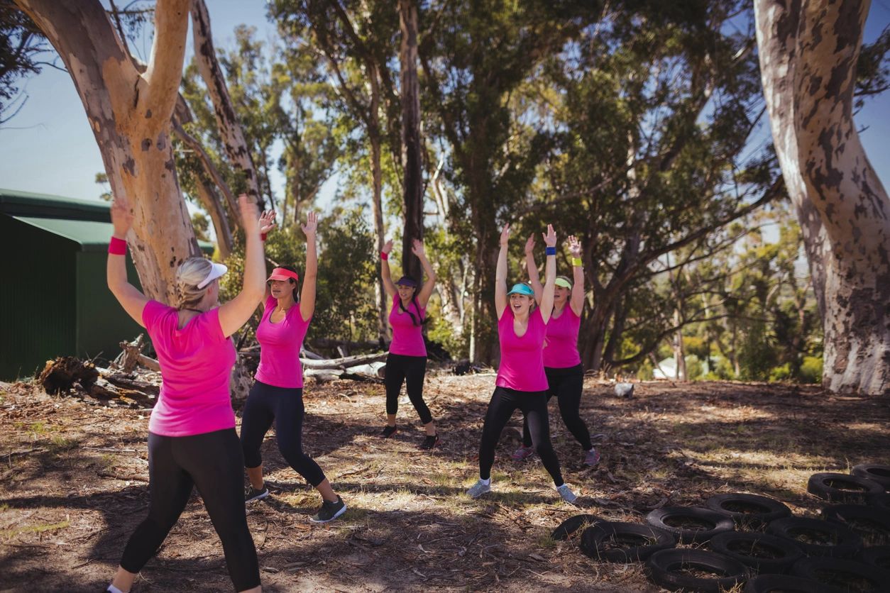 Group exercise outdoors with women raising hands.