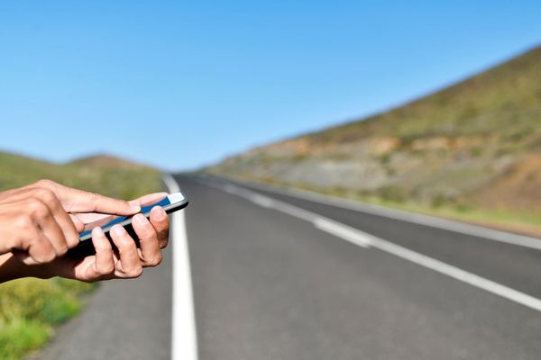 Person using smartphone on the side of an empty road.