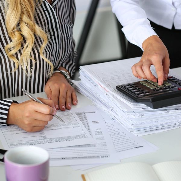 Two people working on paperwork with documents, calculator, and writing tools.