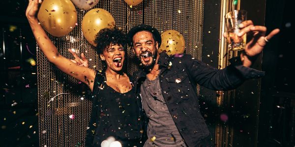 An African-American man and woman celebrating as confetti and gold balloons  are dropping down