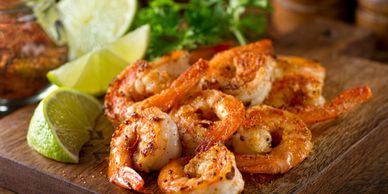 Grilled shrimp served with lime wedges and herbs on a wooden board.