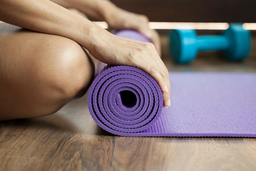 Person rolling up a purple yoga mat with a blue dumbbell in the background.