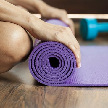 Hands rolling up a yoga mat in a fitness studio.