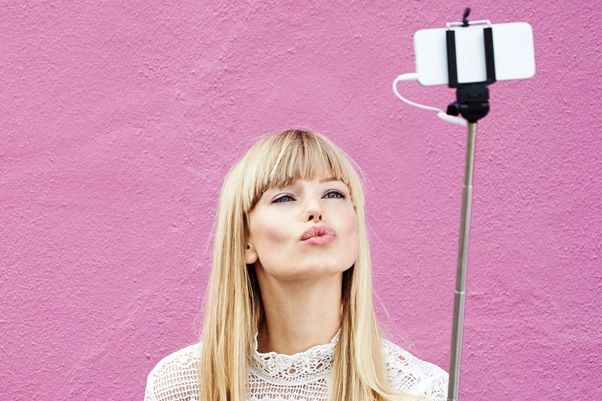 Woman posing for the camera on a selfie stick to demonstrate a tic for TikTok