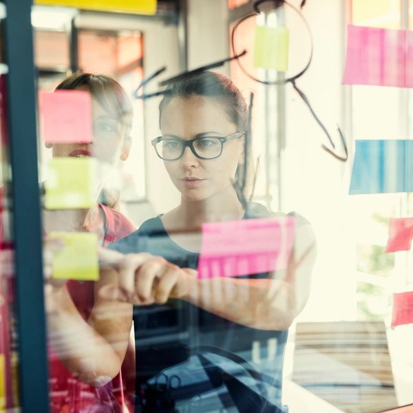 Women brainstorming and putting sticky notes on glass wall