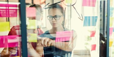 Woman and man using post it notes to review software roadmap on a glass meeting room wall