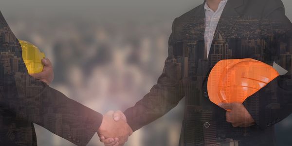 Businessmen shaking hands, holding construction helmets, with cityscape overlay.