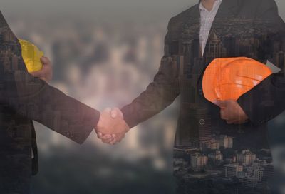 Two professionals shaking hands, one holding an orange safety helmet.