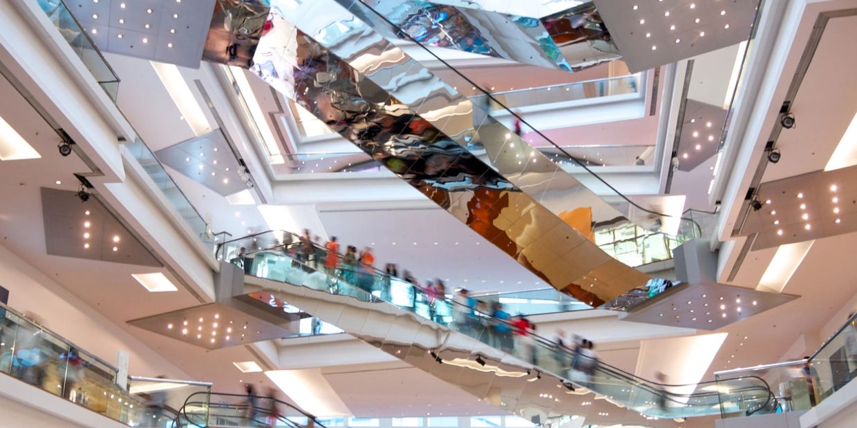 Busy escalators inside a modern shopping mall with reflective surfaces.