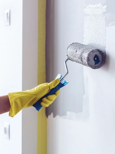 A person wearing yellow gloves painting a white wall with a roller.