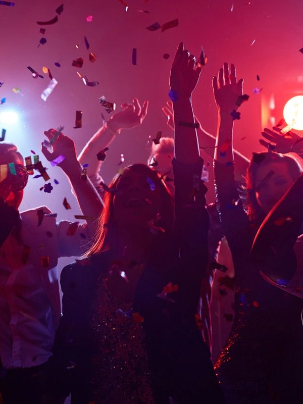 People celebrating with raised hands and confetti in a vibrant party atmosphere.