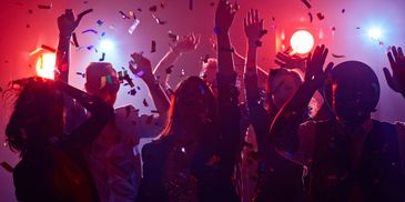 People dancing and celebrating at a lively party with colorful lights and confetti.