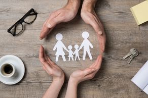 Arial view of two sets of hands encircling a paper cutting silhouette of a family of a family of 4. 