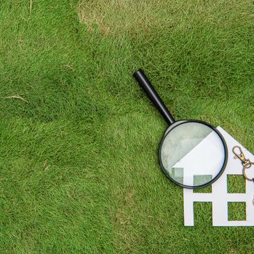 Magnifying glass over white paper house on grass.