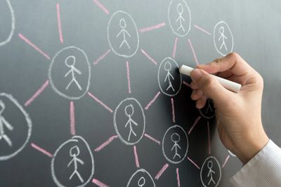 Hand drawing a network of connected stick figures on a blackboard.