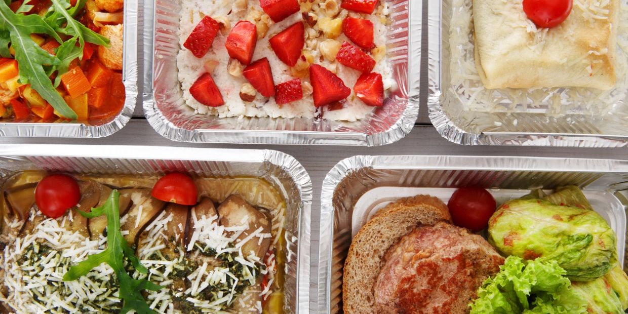 Healthy meal prep trays with vegetables, strawberries, and sandwiches.