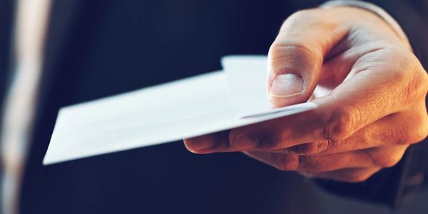 Hand holding and offering white envelopes.