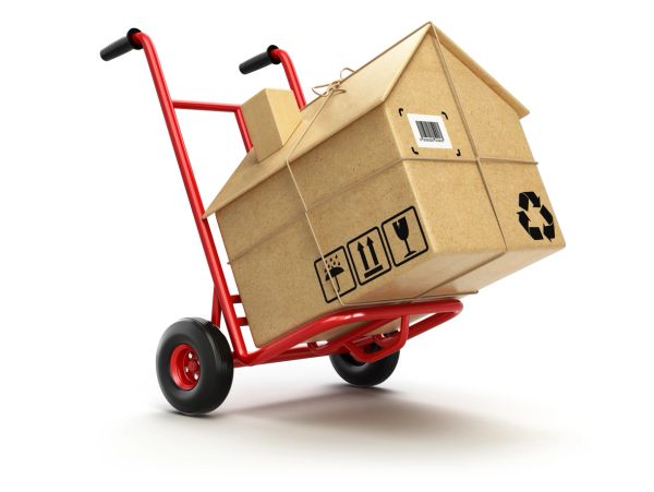 A house-shaped cardboard box on a red hand truck.