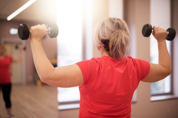 Woman in red shirt lifting dumbbells in a gym.