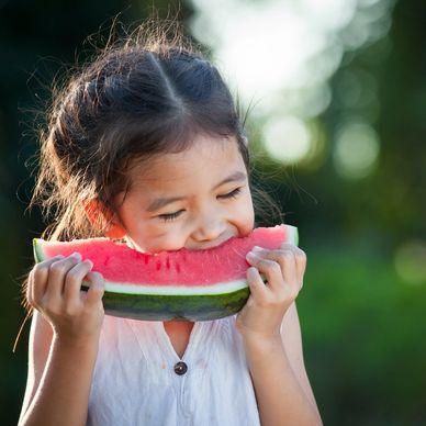 A young girl happily eating a slice of watermelon outdoors.