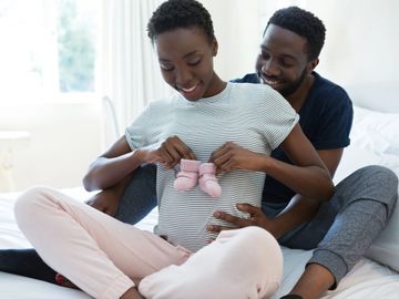 Couple joyfully holding baby shoes over pregnant belly.