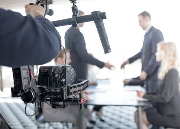 People shaking hands during a business meeting filmed by a camera.