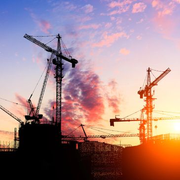 Silhouetted construction cranes against a colorful sunset sky.