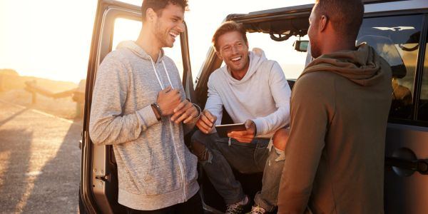Three friends laughing and chatting by a car at sunset.