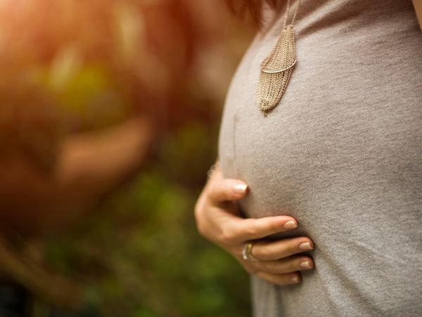 Close-up of a pregnant woman gently holding her belly outdoors.