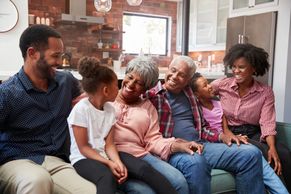 Family unit of 6, 3 generations sitting on couch, smiling at each other.