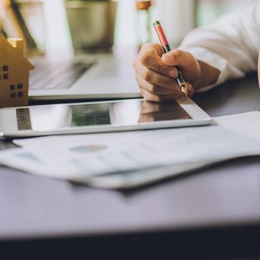 man working on a tablet with a figure of a wooden home and glasses on the desk top.