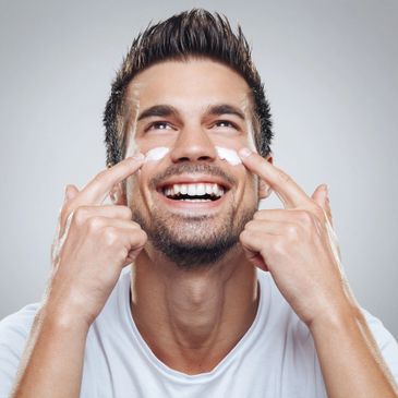 Homme souriant appliquant une crème sur son visage.
