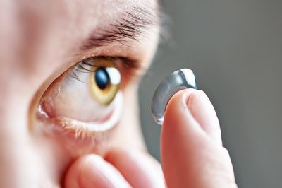 alt = "A person holding a contact lens really close to the eye on an index finger" 