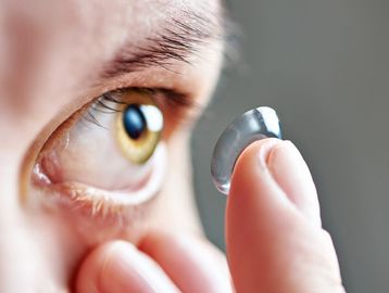 Person holding a contact lens near their eye.