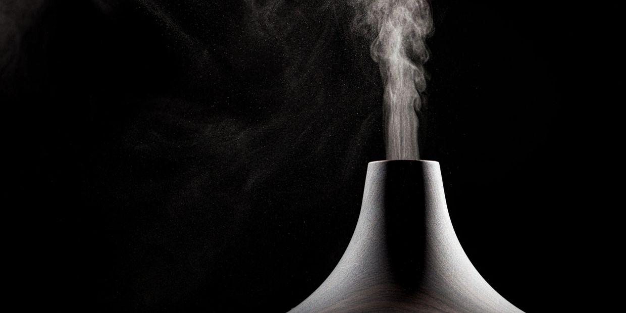 A sleek humidifier emitting vapor against a dark background.
