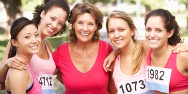 Group of five smiling women with race bibs posing outdoors.