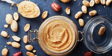 Open jar of creamy peanut butter surrounded by peanuts and peanut shells.
