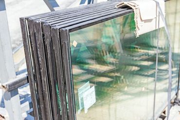 Stack of glass panels leaning against a metal frame outdoors.