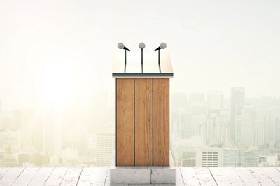 A wooden podium with three microphones, backdrop is a city landscape on a bright sunny day