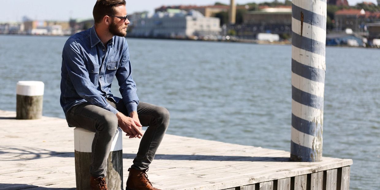 Man in sunglasses sitting on a dock by the water, looking thoughtfully.