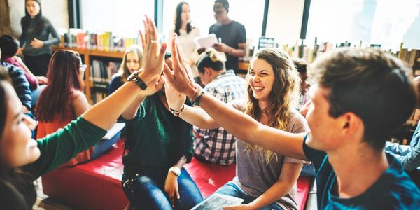 Students sitting in a group study area high-fiving each other and smiling. 