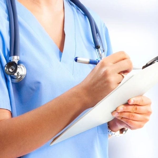 Medical professional in blue scrubs writing on a clipboard.
