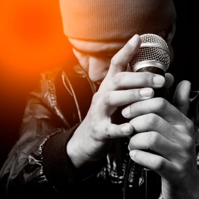 Man in a beanie holding a microphone closely, intense mood.