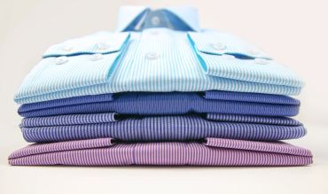 Stack of neatly folded dress shirts in blue and purple tones.