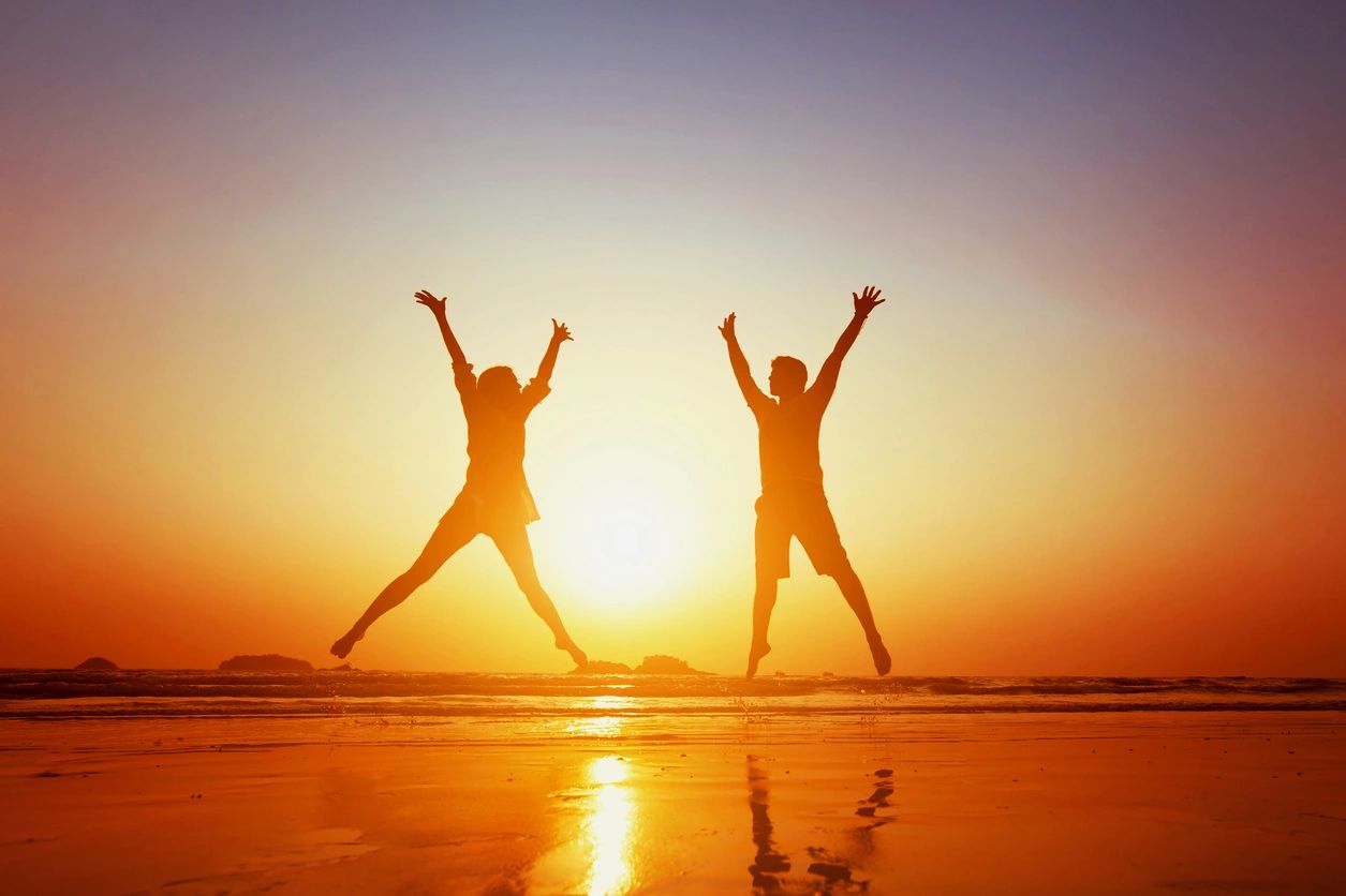 2 silhouetted people jumping in the air with their arms over their heads looking happy and free.