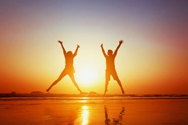 Two people jumping on a beach at sunset.