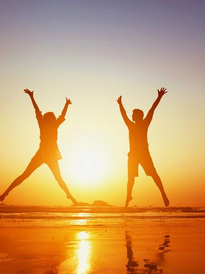 Two people joyfully jump on the beach at sunset.
