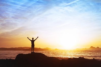 Person looking out into the ocean with arms raised for success